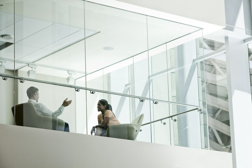 Businessman and woman standing behind a conference room window ina large business center.